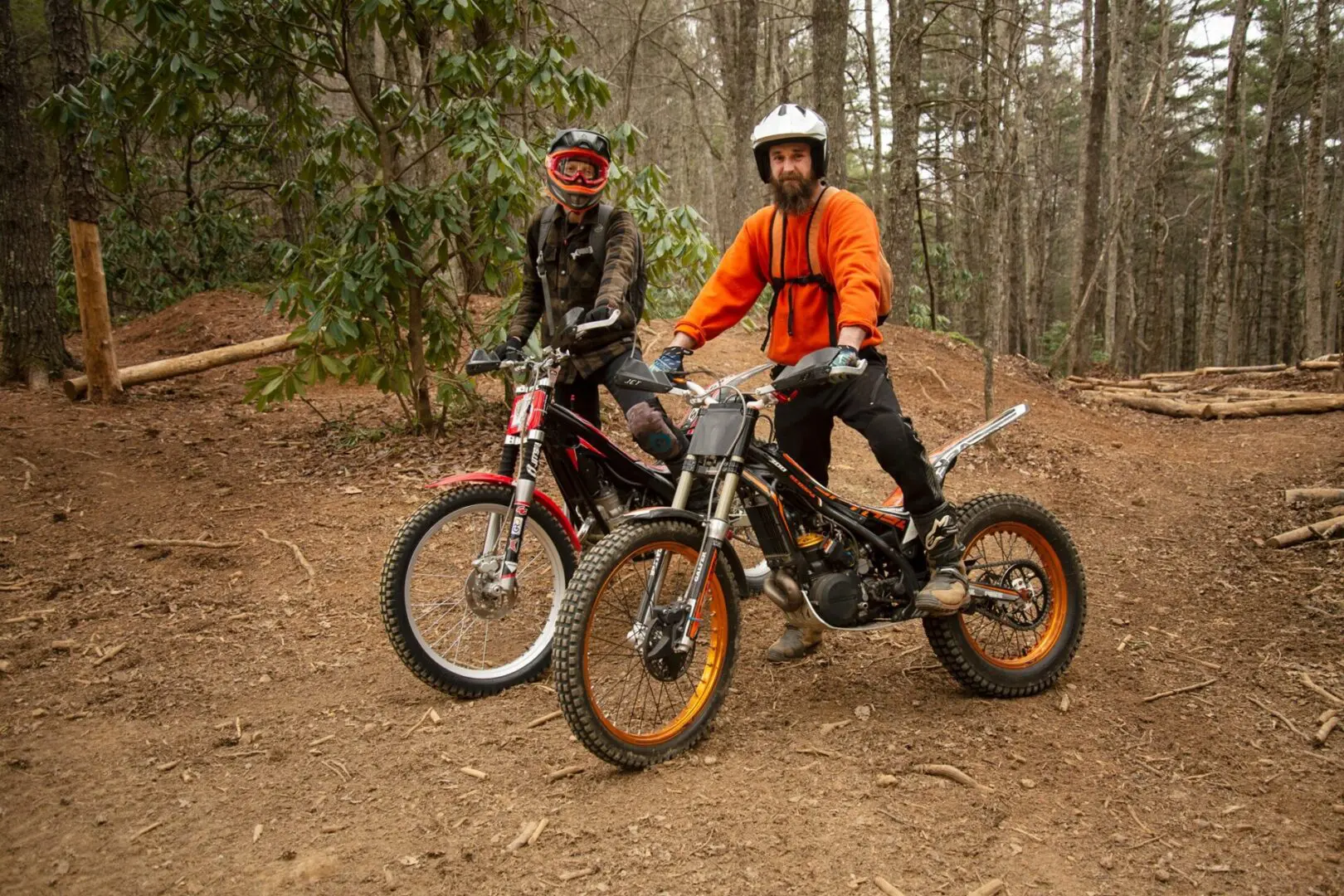 Two people on bikes in the woods near trees.